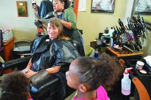 Dawn Herman gets her hair cut by Phylicia McQueen as the stylist’s daughters Anilah and Angalee keep them company.